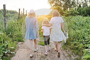 Mother with children two daughters walking along a country road, back view