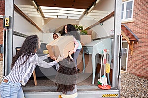 Mother And Children Unloading Furniture From Removal Truck Into New Home