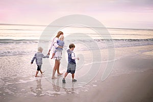 Mother and Children Walking Along Ocean Beach at Sunset