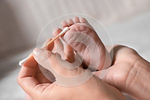 Mother cleaning baby`s foot with cotton bud on blurred background, closeup