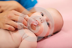 Mother cleaning baby`s mouth with special fingertip brush