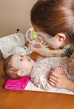 Mother cleaning mucus of baby with nasal aspirator