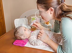 Mother cleaning mucus of baby with nasal aspirator