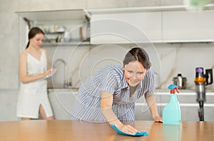 Mother cleaning the table surface, her daughter wiping plates in the kitchen