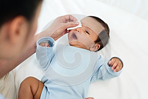 mother cleaning and wiping newborn baby eye with cotton pad on bed