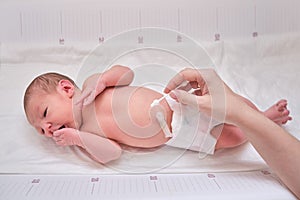 A mother cleans a newborn baby with a cotton swab. A baby in a diaper and mom`s hands with a cotton swab