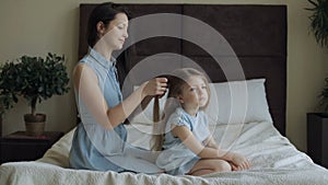 Mother combing daughter hair on bed at home