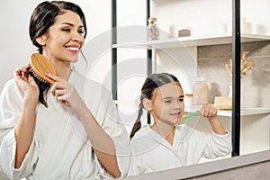 mother combing hair wile daughter brushing teeth photo