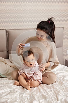 mother is combing her cute little daughter hair on bed