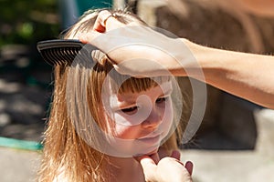 Mother combing her daughters hair, child being combed by her mom using a black comb, closeup, portrait. Woman doing happy little