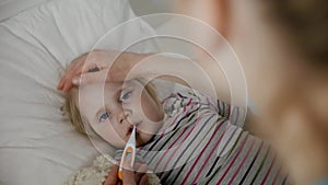 mother comforting her sick child and measuring temperature in bed