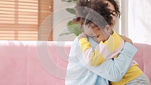 Mother consoling a crying little child and hugging little daughter. Offended black little girl crying on sofa comforting small