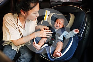 mother consoling newborn baby crying while putting and fasten seat belts on car seat