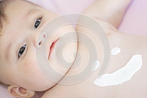 Cute baby with body cream on tummy. Mother creaming