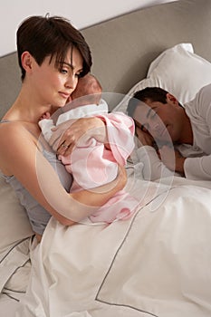 Mother Cuddling Newborn Baby In Bed