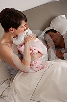 Mother Cuddling Newborn Baby In Bed