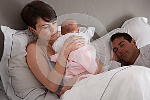 Mother Cuddling Newborn Baby In Bed At Home