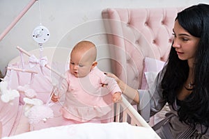 Mother with curious baby playing in pink bedroom.