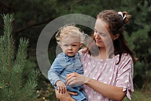 Mother and cute little daughter spending time together on walk in pine tree forest woman holding infant kid in her hands enjoying