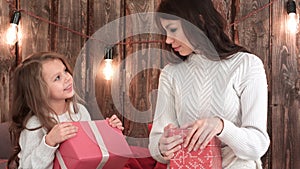 Mother and a cute little girl holding Xmas presents and trying to guess what`s inside