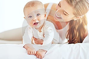 Mother and cute, newborn baby boy bonding together as a family in the bedroom at home. Happy, smiling and carefree mom