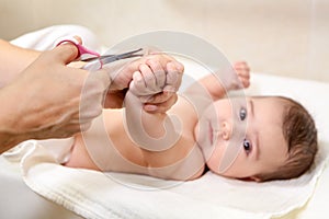 Mother cuts fingernails of her newborn baby boy, calm child lying back and looking at camera