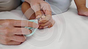 mother cutting baby's foot fingernails with nail scissors.