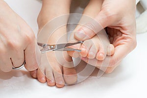 Mother cutting fingernails on the feet of her child using nail scissors.