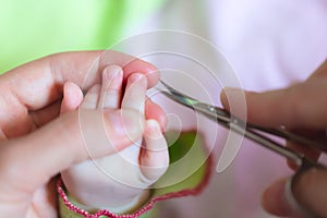 Mother is cutting tiny nails neatly and gently on the hand of newborn using nail scissors . Concept of care mom for baby