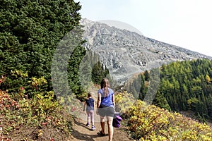 A mother and daugher hiking a beautiful trail above the treeline with a huge mountain in the background during a sunny fall day