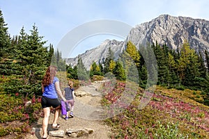 A mother and daugher hiking a beautiful trail above the treeline with a huge mountain in the background during a sunny fall day