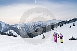 Mother with daugher walking hand in hand by snow moontain trail. Active outdoor time spending concept image