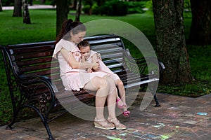 Mother and daughter 5-6 years old walk in the Park in the summer, mother hugs her daughter sitting on a bench, the concept of a