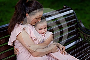 Mother and daughter 5-6 years old walk in the Park in the summer, mother hugs her daughter sitting on a bench, the concept of a