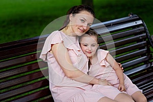 Mother and daughter 5-6 years old walk in the Park in the summer, mother hugs her daughter sitting on a bench, the concept of a