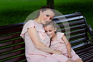 Mother and daughter 5-6 years old walk in the Park in the summer, mother hugs her daughter sitting on a bench, the concept of a