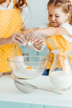Mother and daughter adding smashed egg to flour in bowl while cooking together