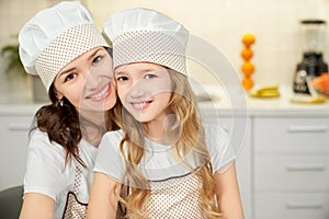 Mother and daughter in aprons and chef hats posing, smiling.