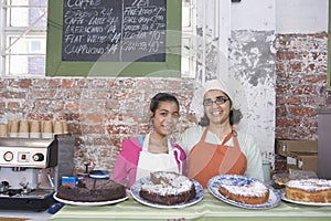 Mother And Daughter In Aprons Standing At Cake Shop Counter