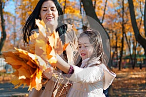 Mother and daughter are in autumn city park, happy people walking together, family with children, playing with yellow leaves,