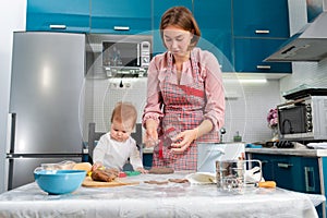 Mother and daughter baby prepare gingerbread together. Mother& x27;s Day concept and cooking festive home-cooked meals