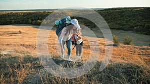 Mother and daughter with backpacks running through the meadow at sunset. Family tourism concept.