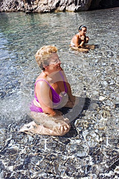 Mother and daughter bathing in crystal clear water at a pebble beach.