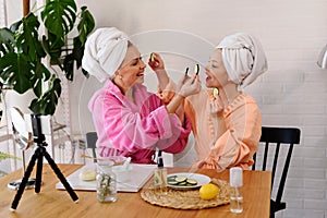 Mother and daughter in bathrobes and towels on head using natural cosmetics and having fun