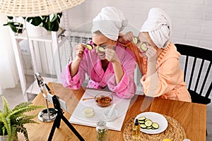 Mother and daughter in bathrobes and towels on head using natural cosmetics and having fun