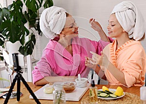 Mother and daughter in bathrobes and towels on head using natural cosmetics and having fun