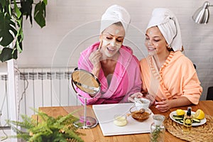 Mother and daughter in bathrobes and towels on head using natural cosmetics and having fun