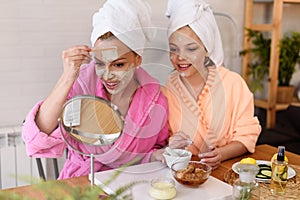 Mother and daughter in bathrobes and towels on head using natural cosmetics and having fun