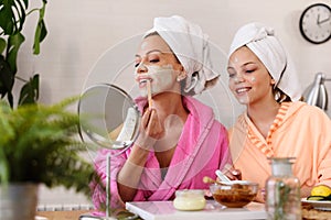 Mother and daughter in bathrobes and towels on head using natural cosmetics and having fun