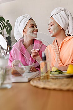 Mother and daughter in bathrobes and towels on head using natural cosmetics and having fun